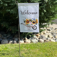 White garden flag with "Welcome" and a wheelbarrow with a sunflower bouquet on it 